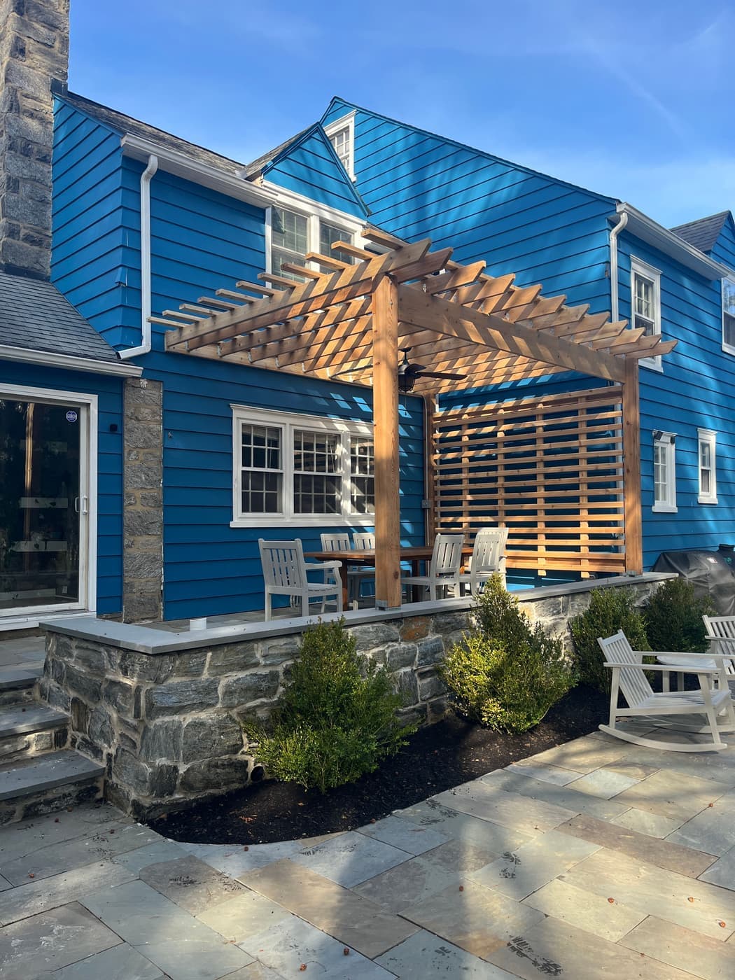 Bluestone patio and cedar pergola behind a blue clapboard home