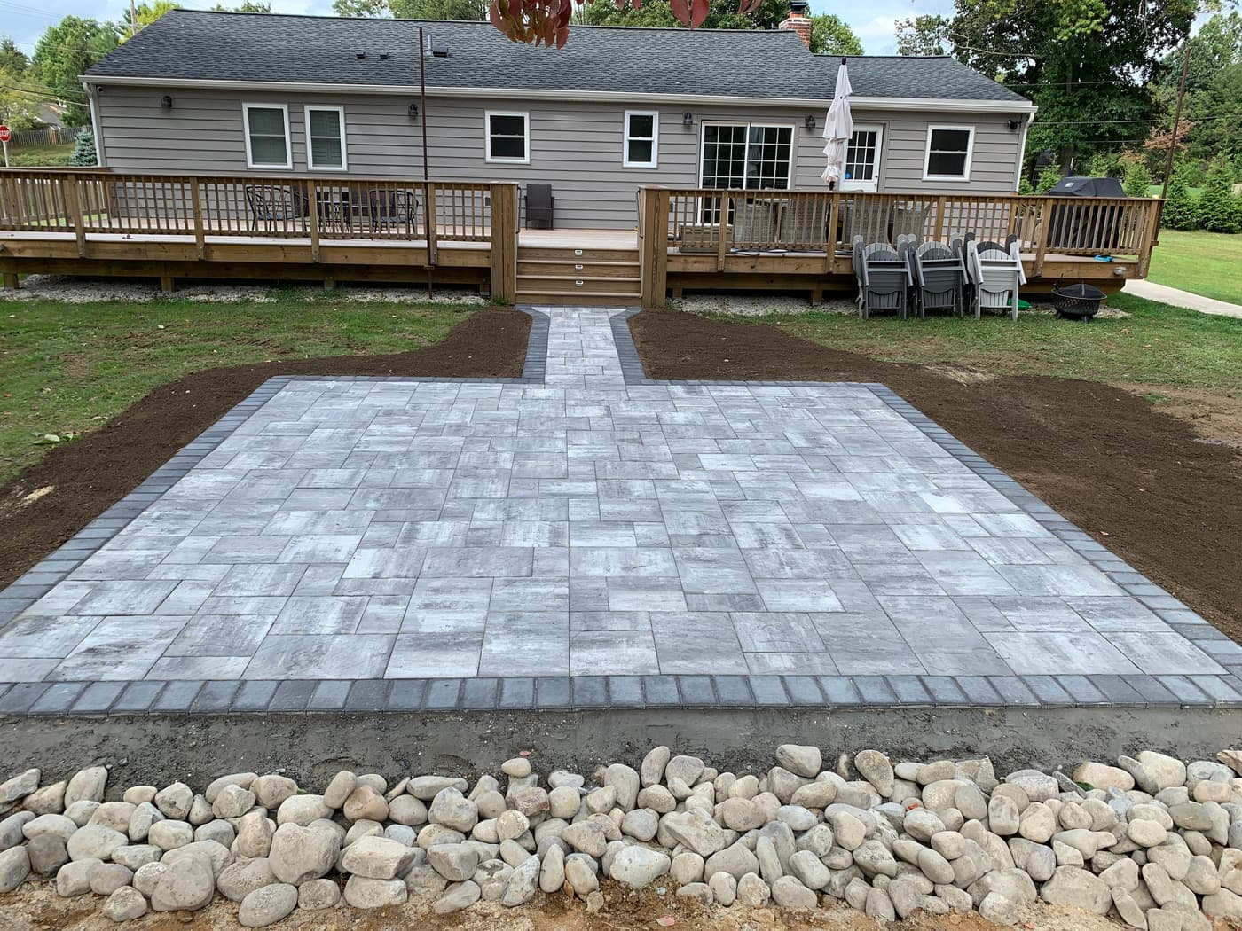 Large gray paver patio with a central walkway and river-rock border