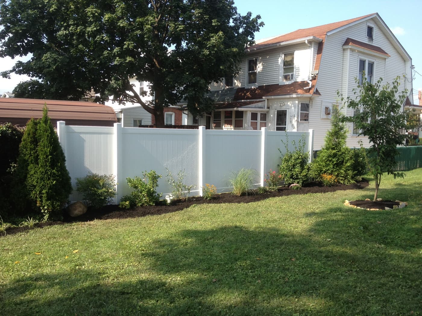 Vinyl privacy fence with newly mulched garden beds and plantings